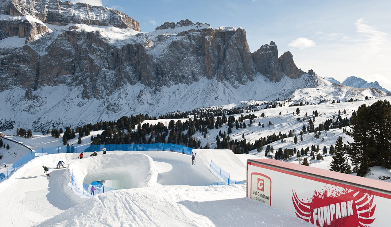 Parco neve FUNPARK con snowboarder su piste innevate, davanti a imponenti pareti rocciose delle Dolomiti