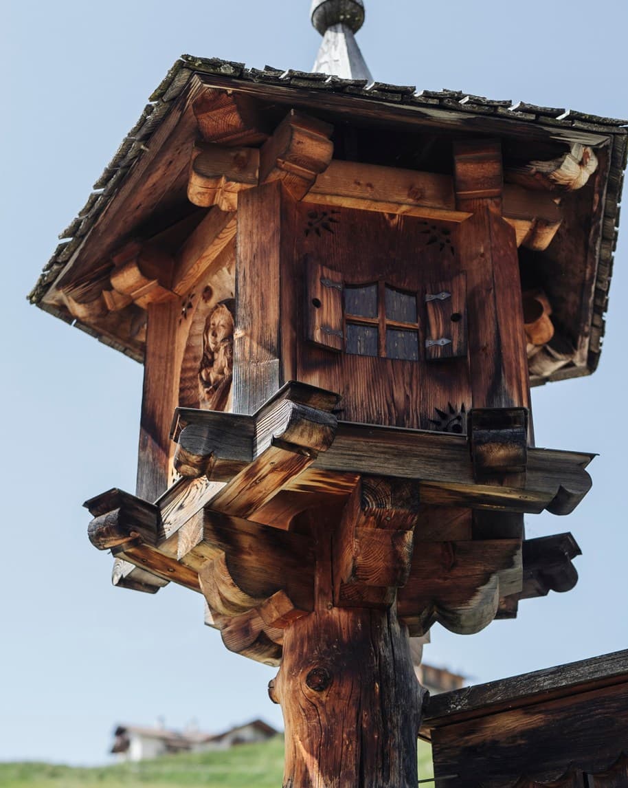 Casetta in legno su palo con finestrella a sportelli e tetto spiovente, sfondo collinare