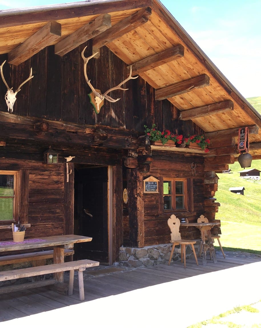 Chalet in legno con corna di cervo sulla facciata, fioriere con gerani rossi, panca e sedie esterne