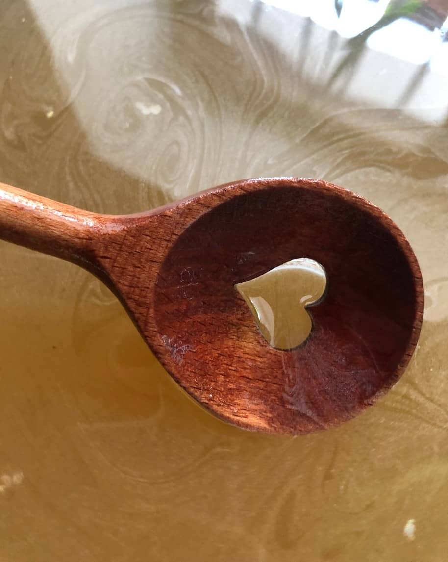 Cucchiaio di legno con goccia a forma di cuore al centro, appoggiato su superficie marmorizzata