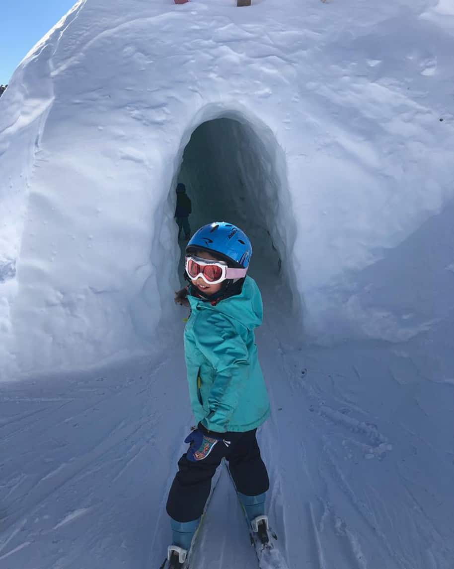 Bambina con casco e sci davanti all'ingresso di un tunnel scavato nella neve