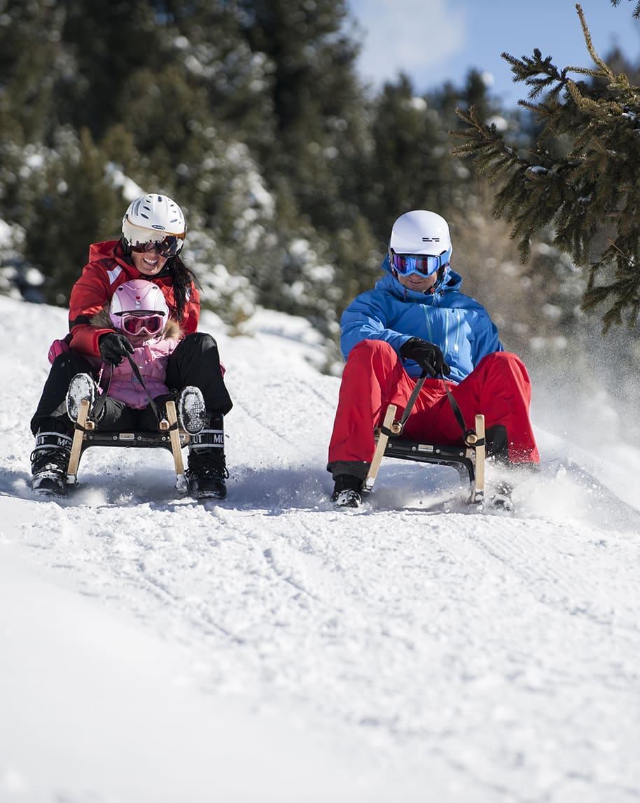 Adulto e bambino su slitta a sinistra, adulto su slitta a destra, entrambi scendono su neve