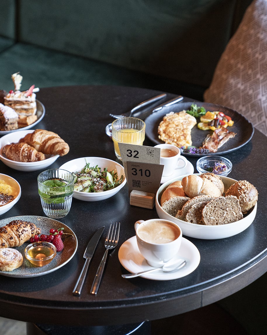 Colazione su tavolo rotondo: tazze di caffè, succo, croissant, pane, insalata, omelette