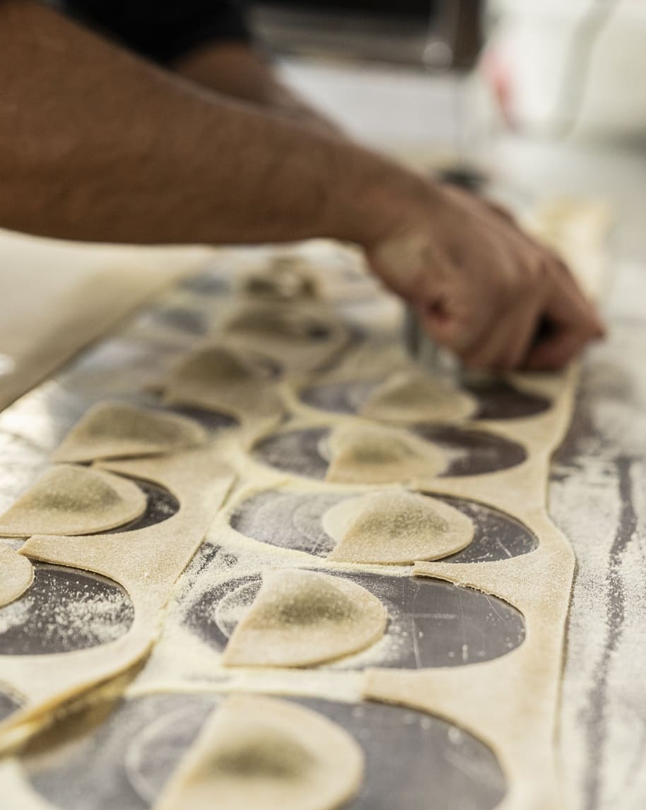 Mano che ritaglia ravioli da una sfoglia su piano infarinato, file di ravioli in primo piano