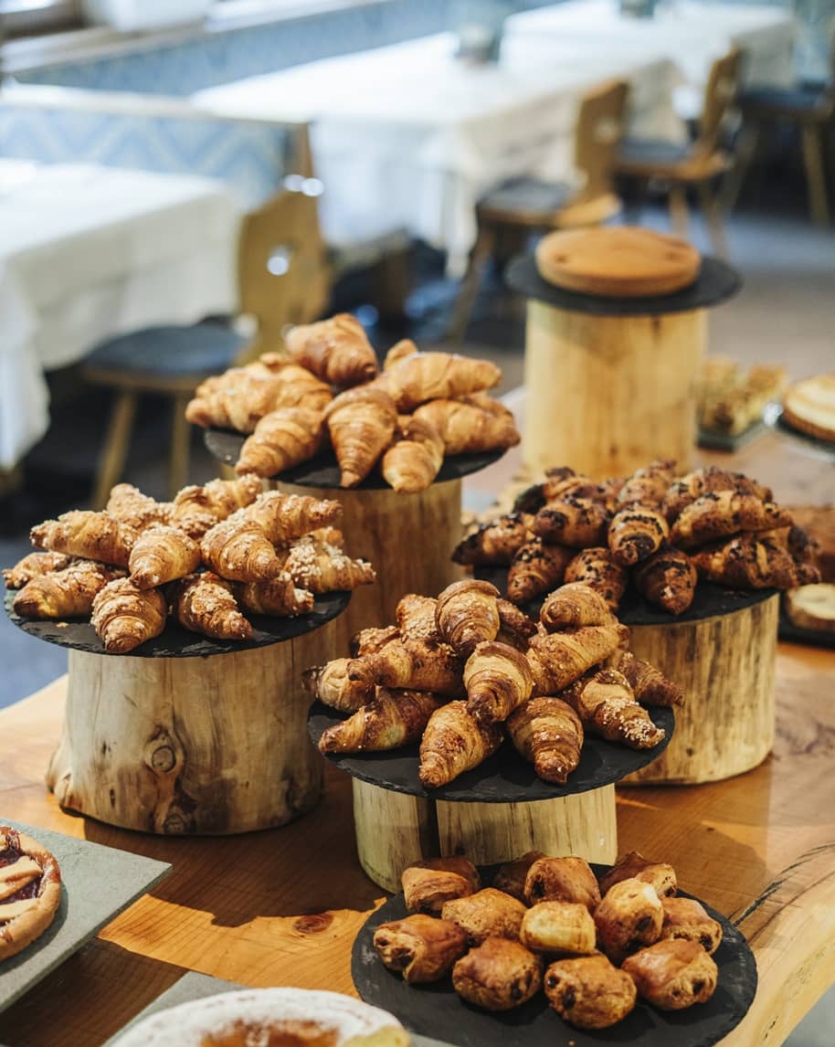 Vassoi su tronchi con croissant e sfogliatine impilati su tavolo da buffet in sala con tavoli e sedie