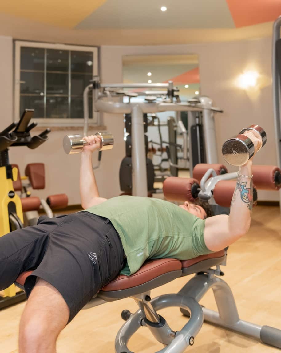 Persona sdraiata su panca in palestra solleva due manubri per distensioni