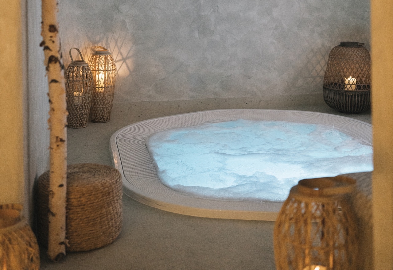 Vasca idromassaggio con acqua schiumosa illuminata e lanterne con candele in ambiente caldo