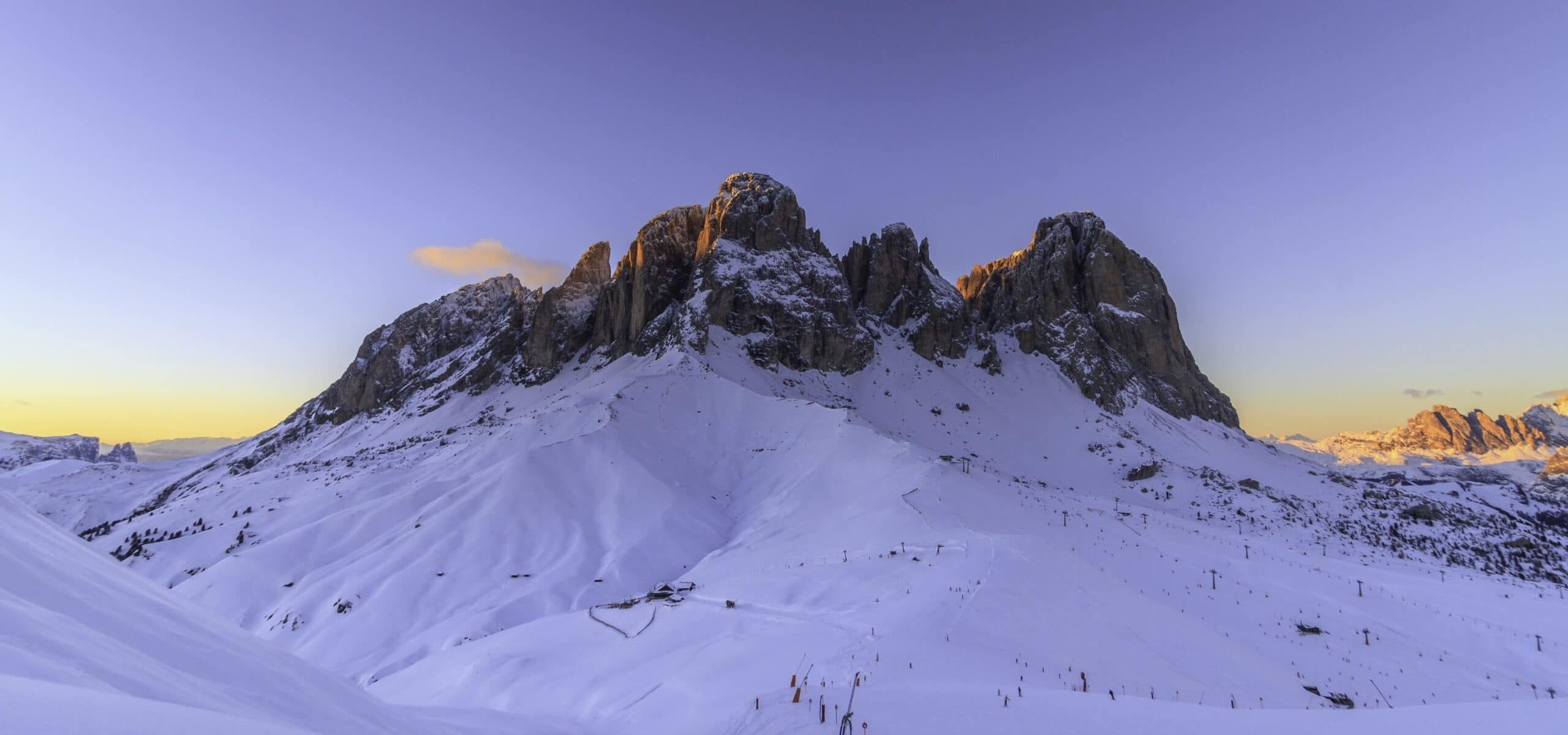 Catena montuosa innevata al tramonto con cime illuminate, pendii sciabili e impianti di risalita
