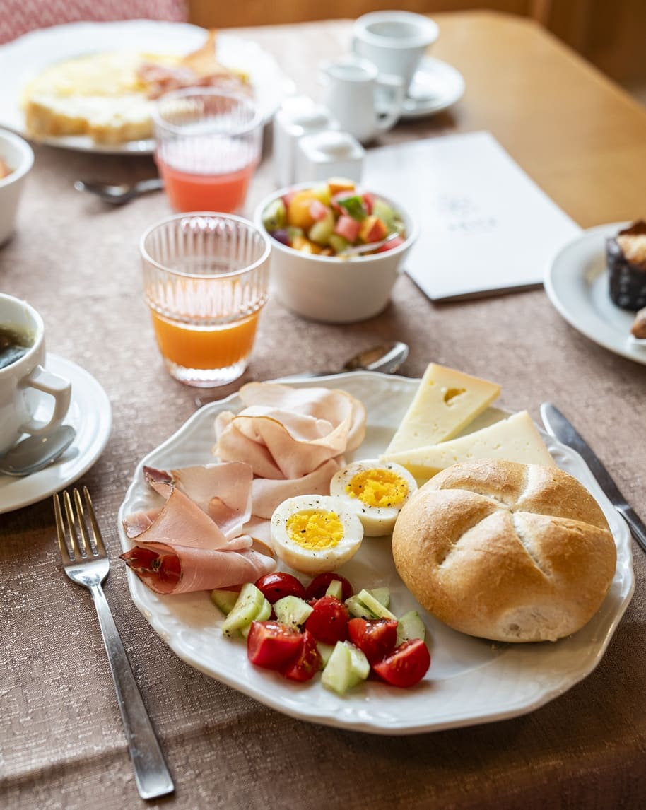 Piatto con panino, uova sode, formaggi, prosciutto e insalata di pomodorini su tavola da colazione