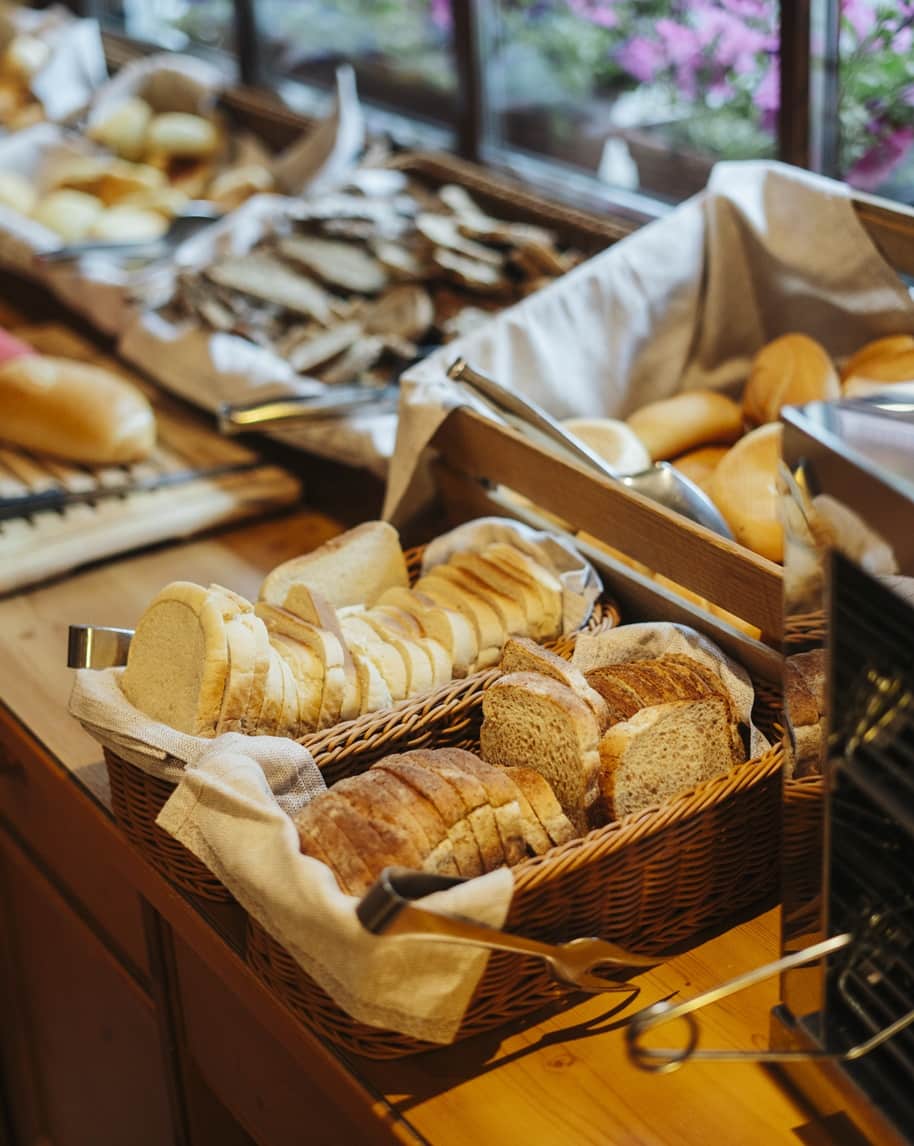 Cesti su buffet con fette di pane affettato, pinze e vassoi di panini su tavolo in legno