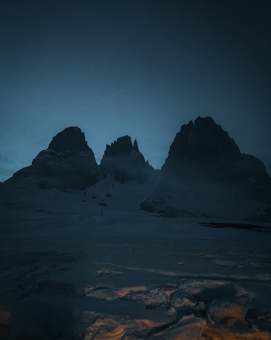 Tre cime rocciose al crepuscolo su pianoro innevato; neve in primo piano illuminata da luce calda