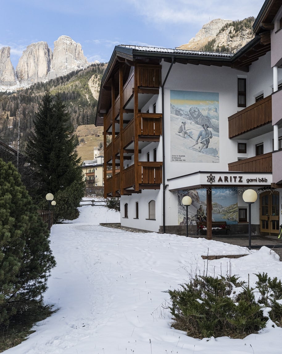 Edificio ARITZ garni b&b con balconi in legno e murale, sentiero nella neve e montagne sullo sfondo