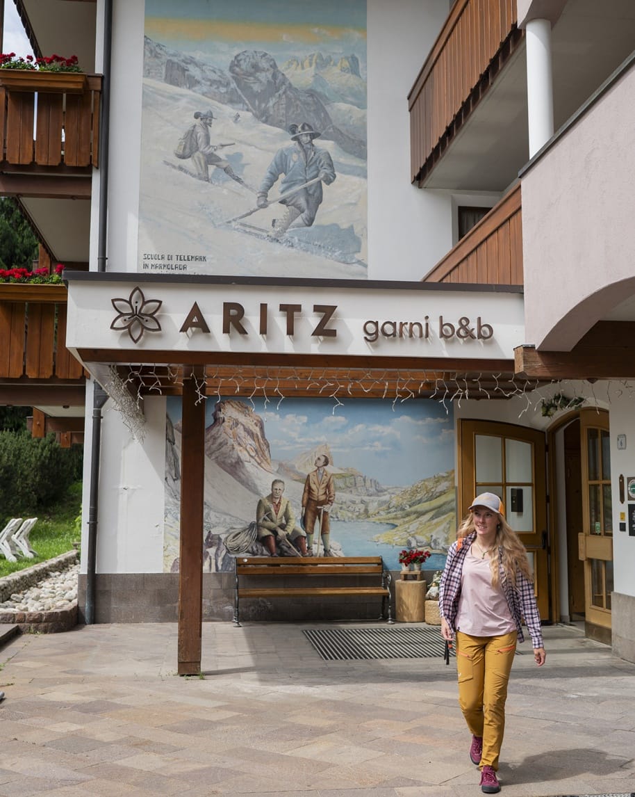 Ingresso ARITZ Garni B&B con murale montano sullo sfondo; donna che cammina in primo piano.