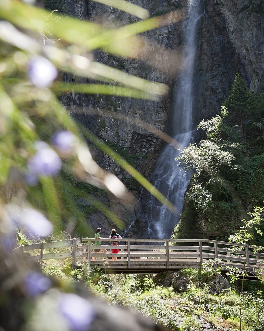 Cascata su parete rocciosa; due persone su ponte di legno che la osservano