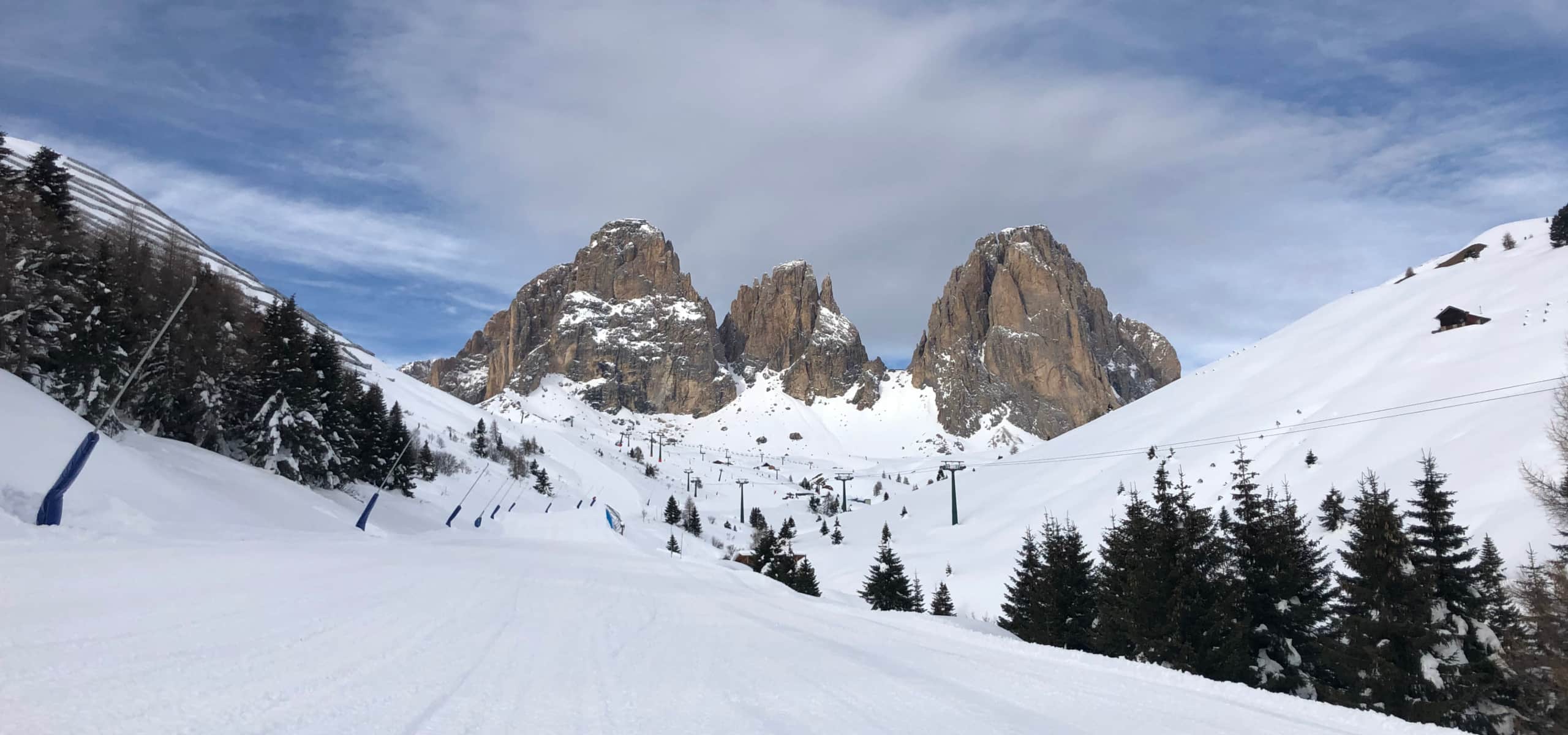 Tre massicci pinnacoli rocciosi sullo sfondo, piste innevate con seggiovie, alberi e una baita sulla destra