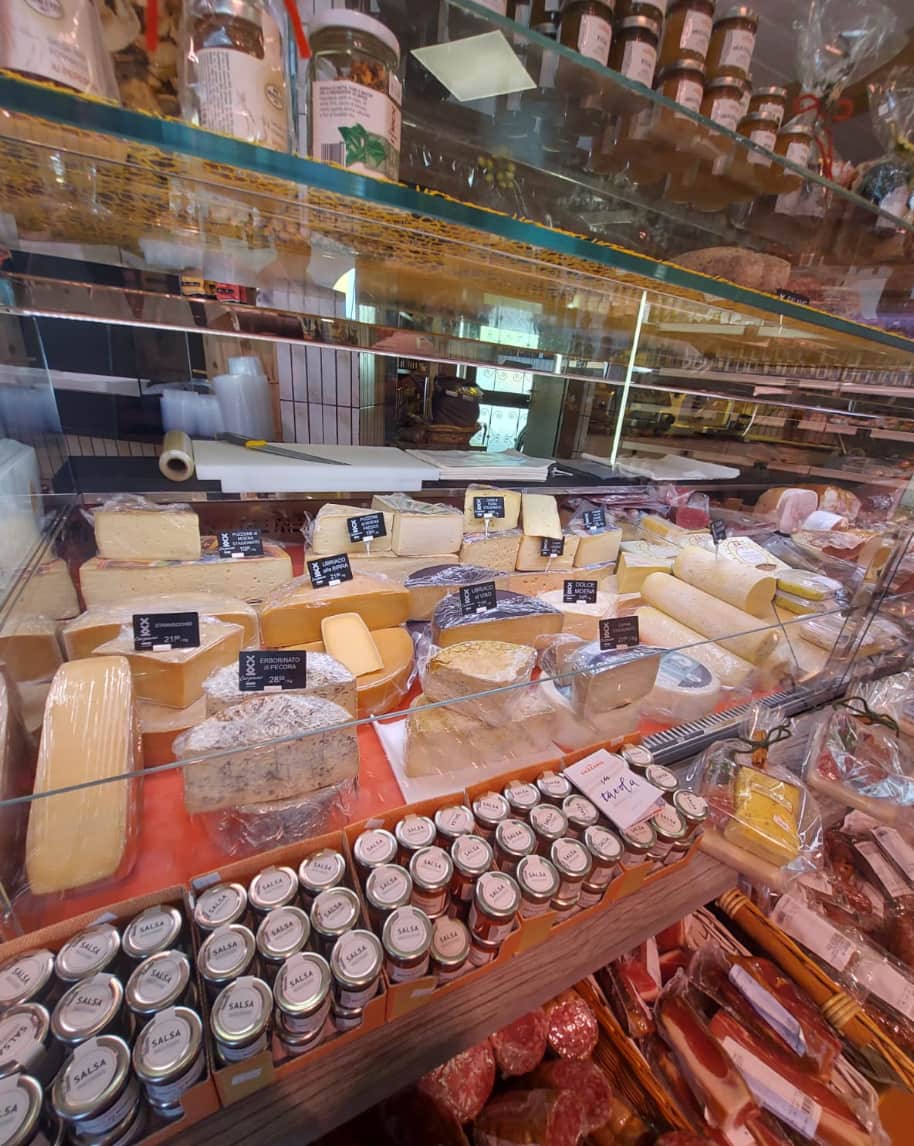 Banco salumeria con forme di formaggio esposte, vasetti in primo piano e salumi sotto il bancone