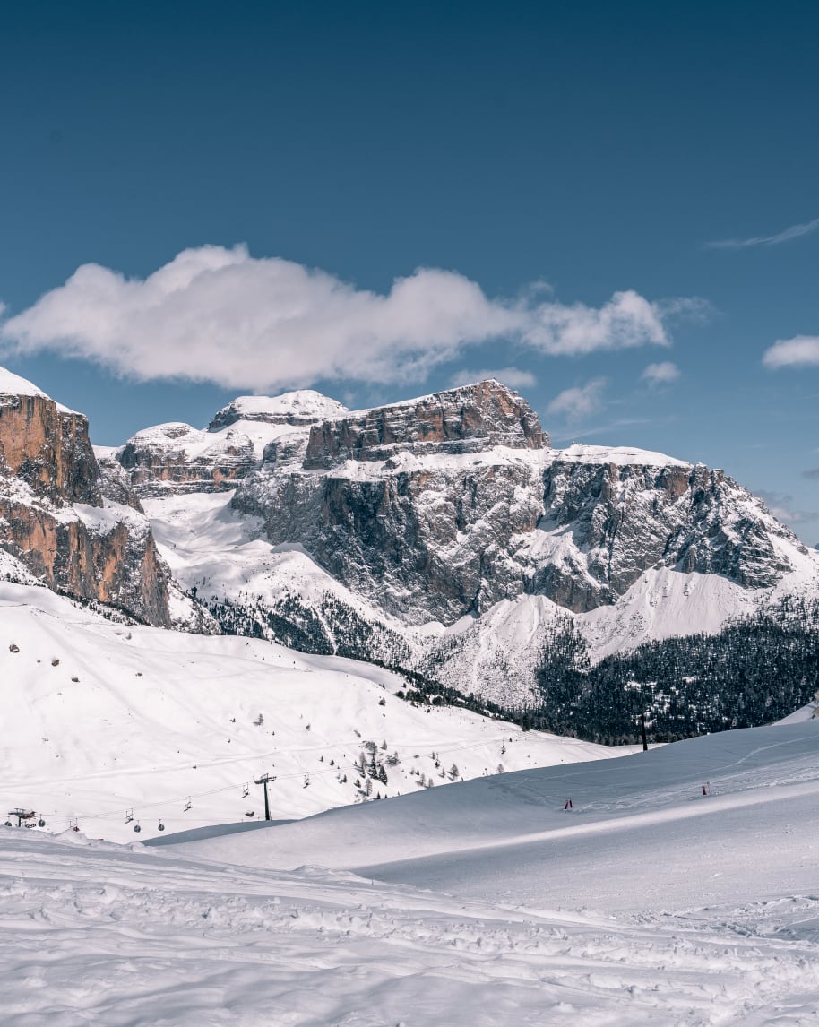 Massicce pareti rocciose innevate, ampi pendii con seggiovia sotto cielo sereno