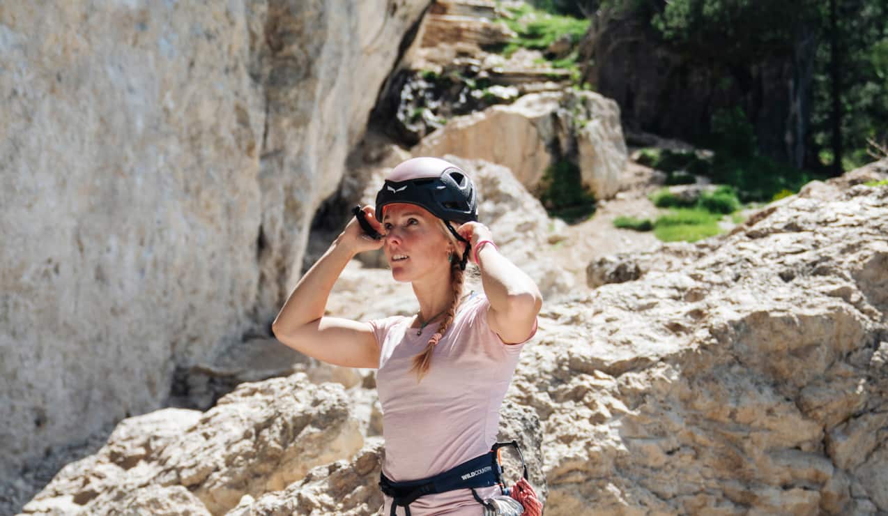 Persona che si sistema il casco da arrampicata davanti a una parete rocciosa