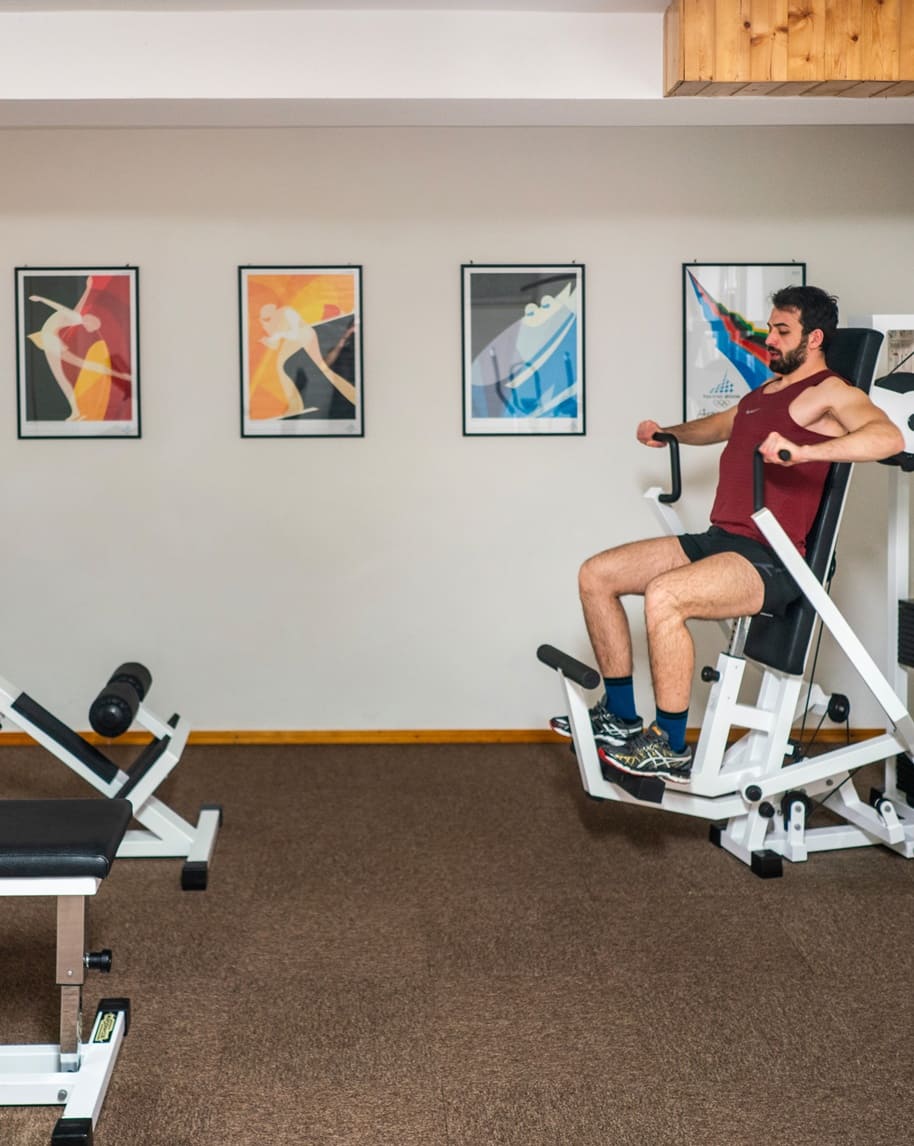 Uomo su macchina da palestra che spinge le maniglie, sfondo con quattro quadri appesi