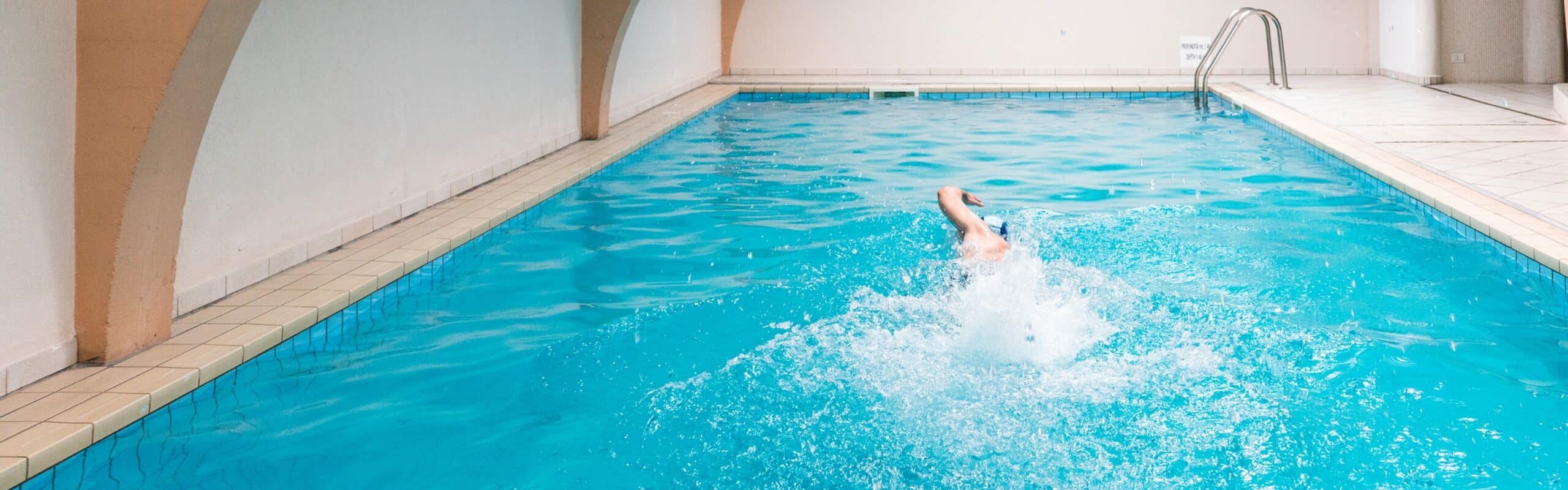 Persona che nuota a stile libero in piscina coperta, spruzzi e scia d'acqua