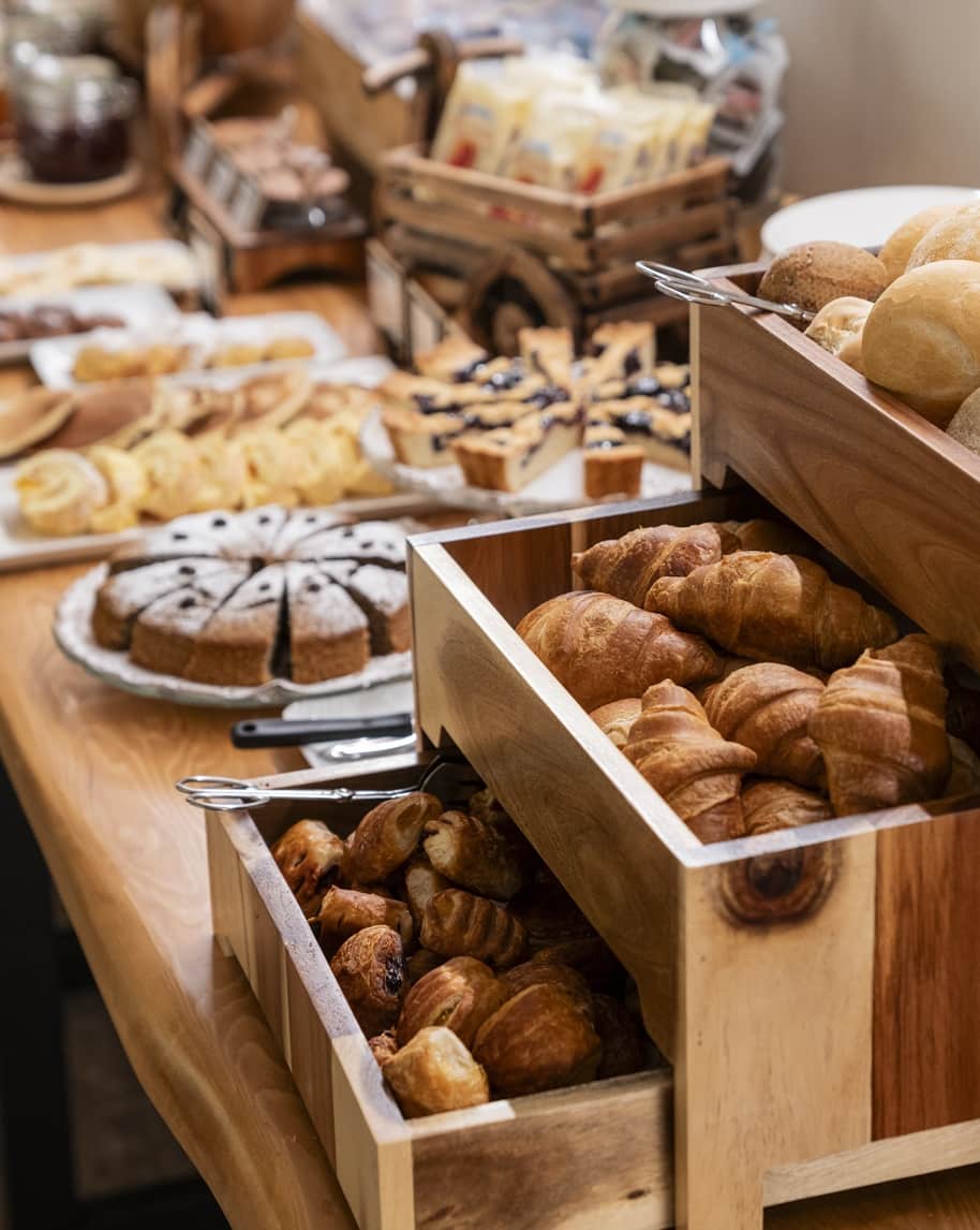 Cestelli di legno con croissant, panini e cornetti su tavolo buffet con torte e dolci sullo sfondo