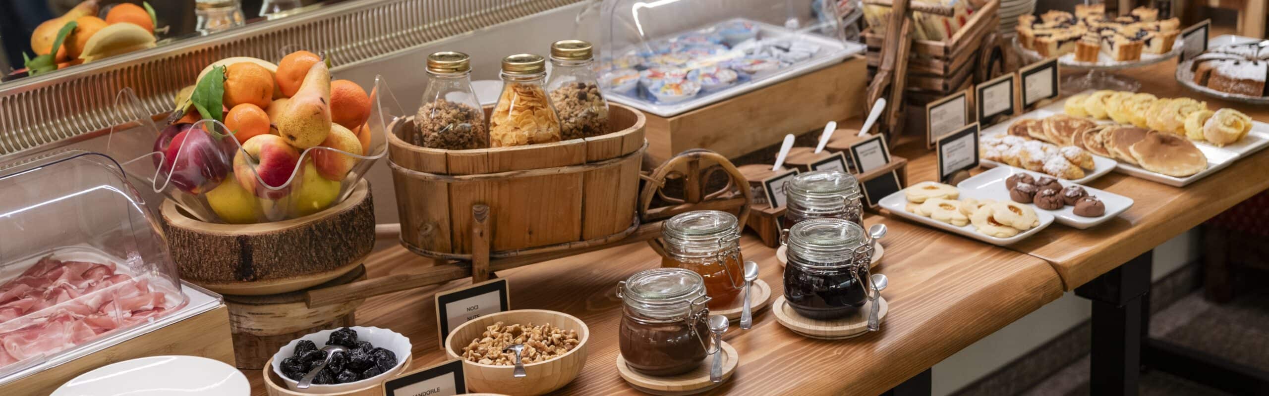 Banco buffet con frutta, cereali in vasetti, marmellate e pasticceria su tavolo in legno