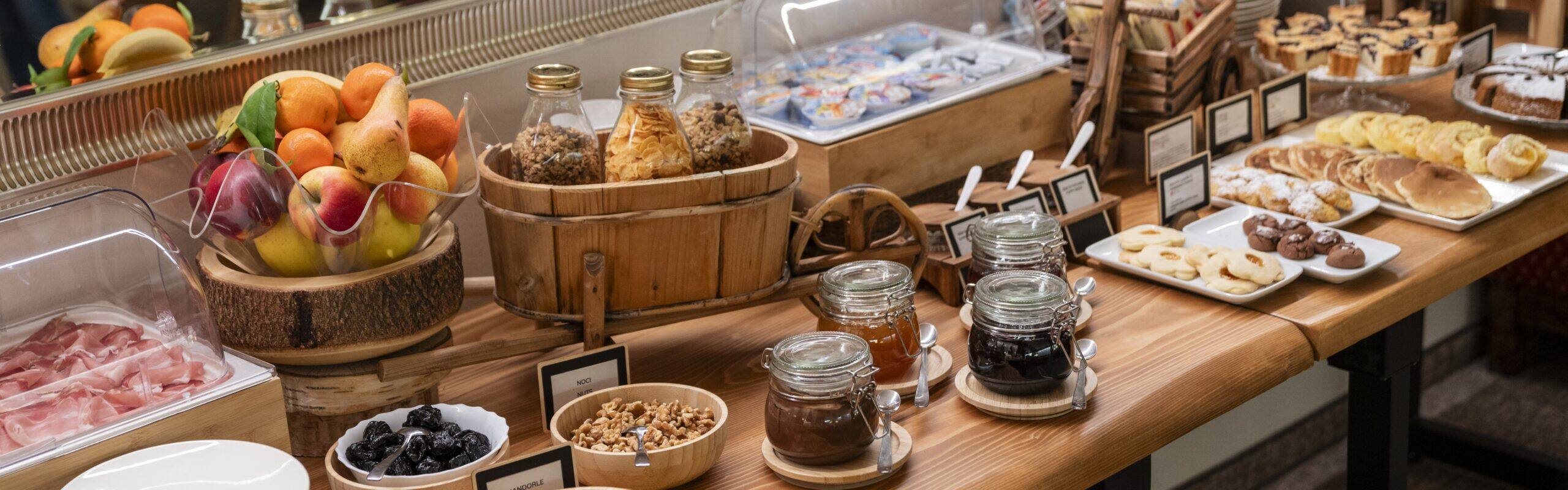 Buffet colazione: frutta, cereali in barattoli, marmellate in vasetti, biscotti e pancake su tavolo