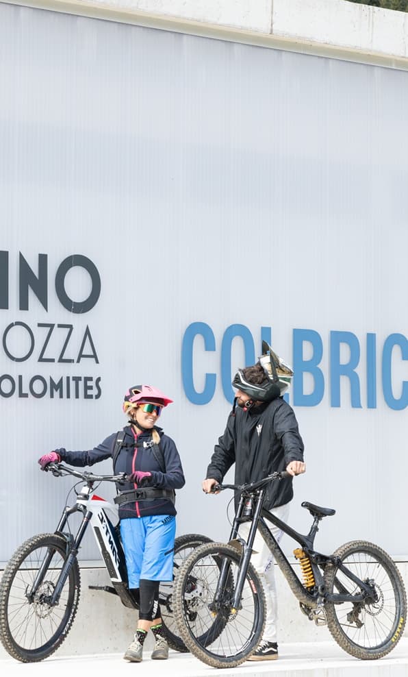 Due ciclisti in casco e abbigliamento da mountain bike, in piedi con le bici davanti a un muro con scritte