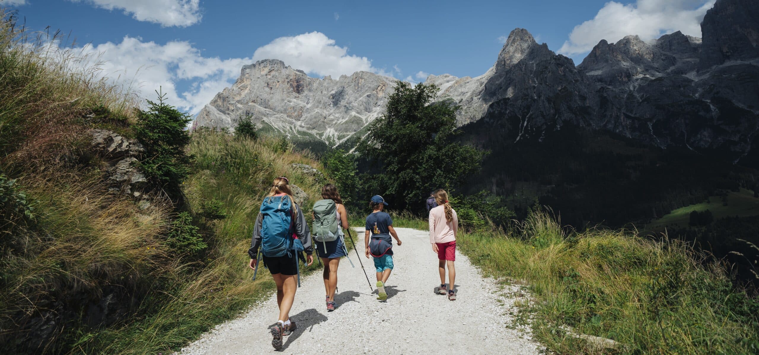Quattro escursionisti camminano su un sentiero di ghiaia verso cime rocciose in montagna