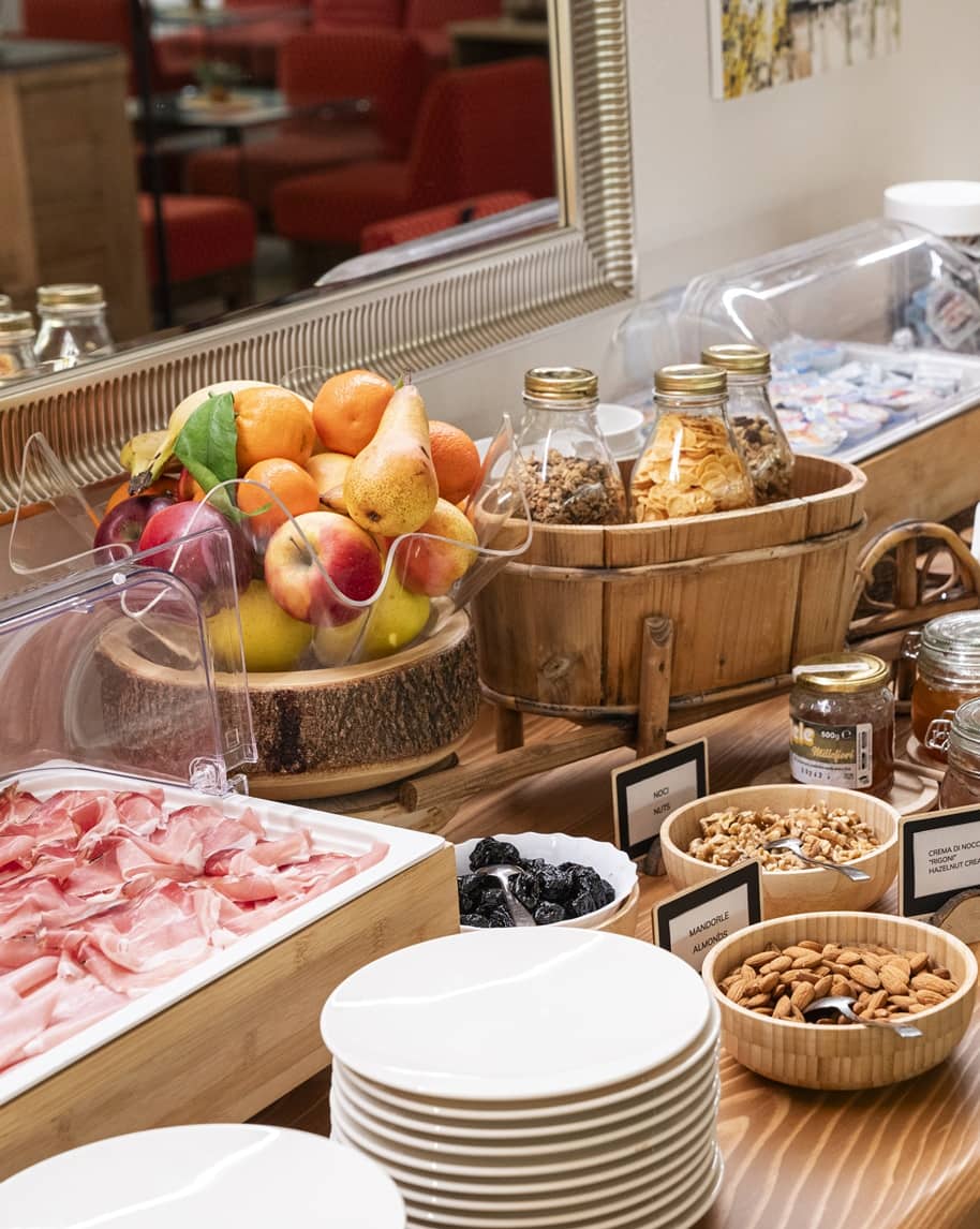 Banco colazione con frutta in ciotola, barattoli di cereali, ciotole di noci e affettati su piatti