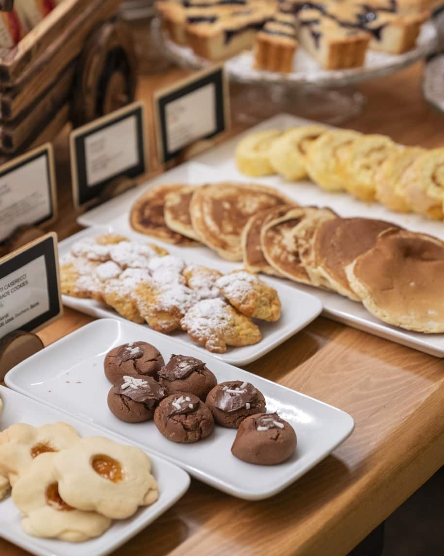 Vassoio su tavolo con pancake, biscotti al cioccolato, frollini con marmellata e pasticcini spolverati di zucchero