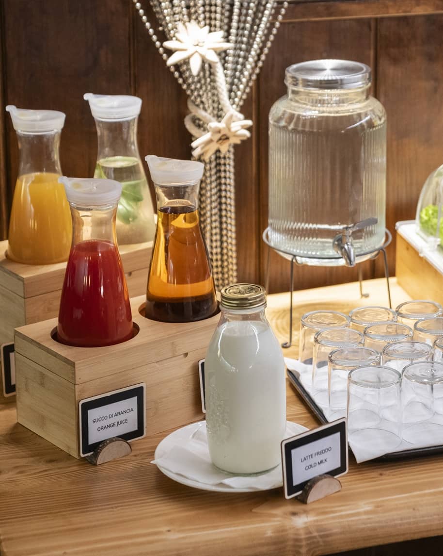 Bottiglia con etichetta 'Latte freddo' su piatto, caraffe di succhi (succo d'arancia) e dispenser d'acqua con bicchieri