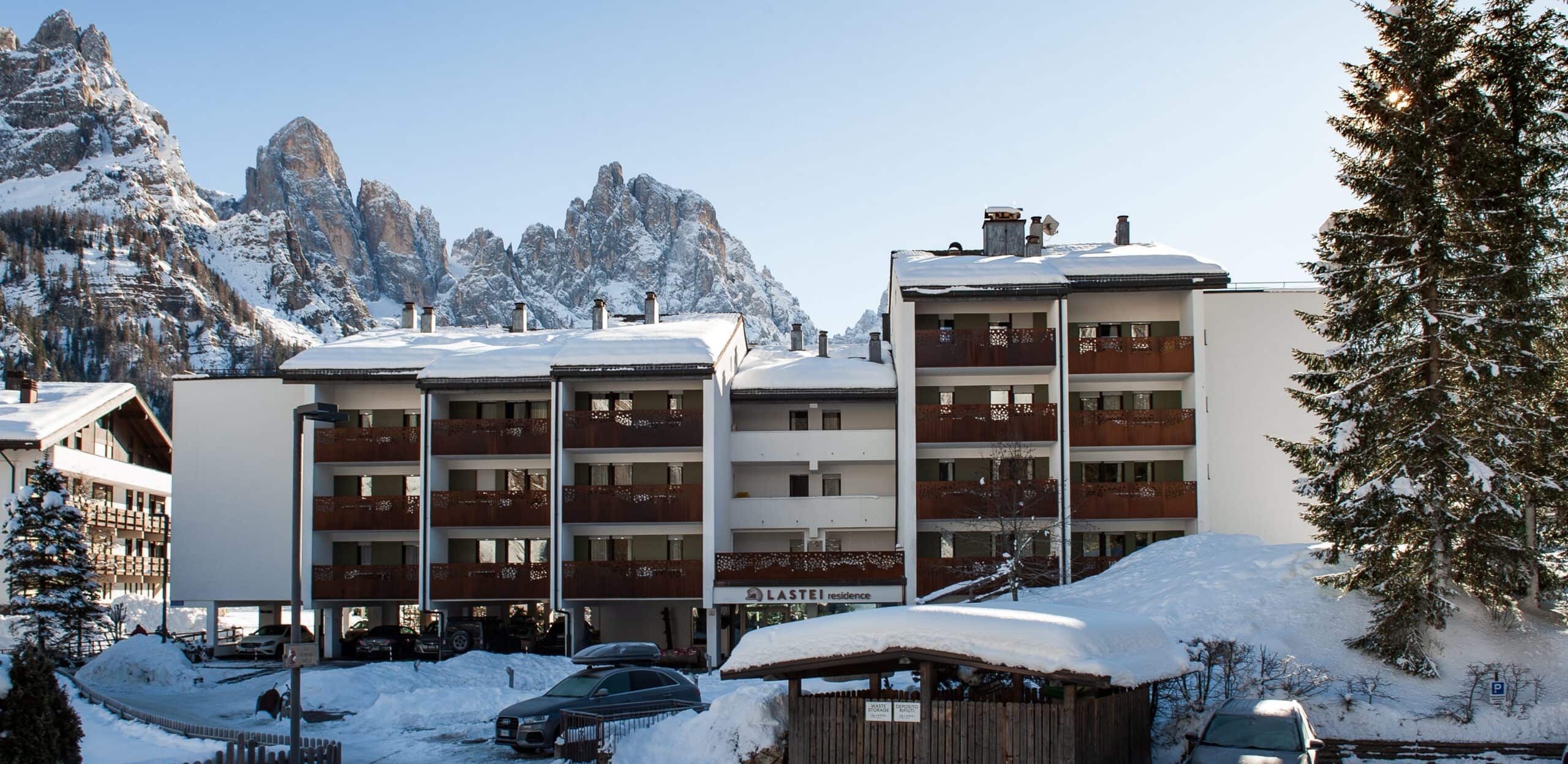 Edificio residence Lastei con balconi di legno, neve sulle terrazze e montagne rocciose sullo sfondo