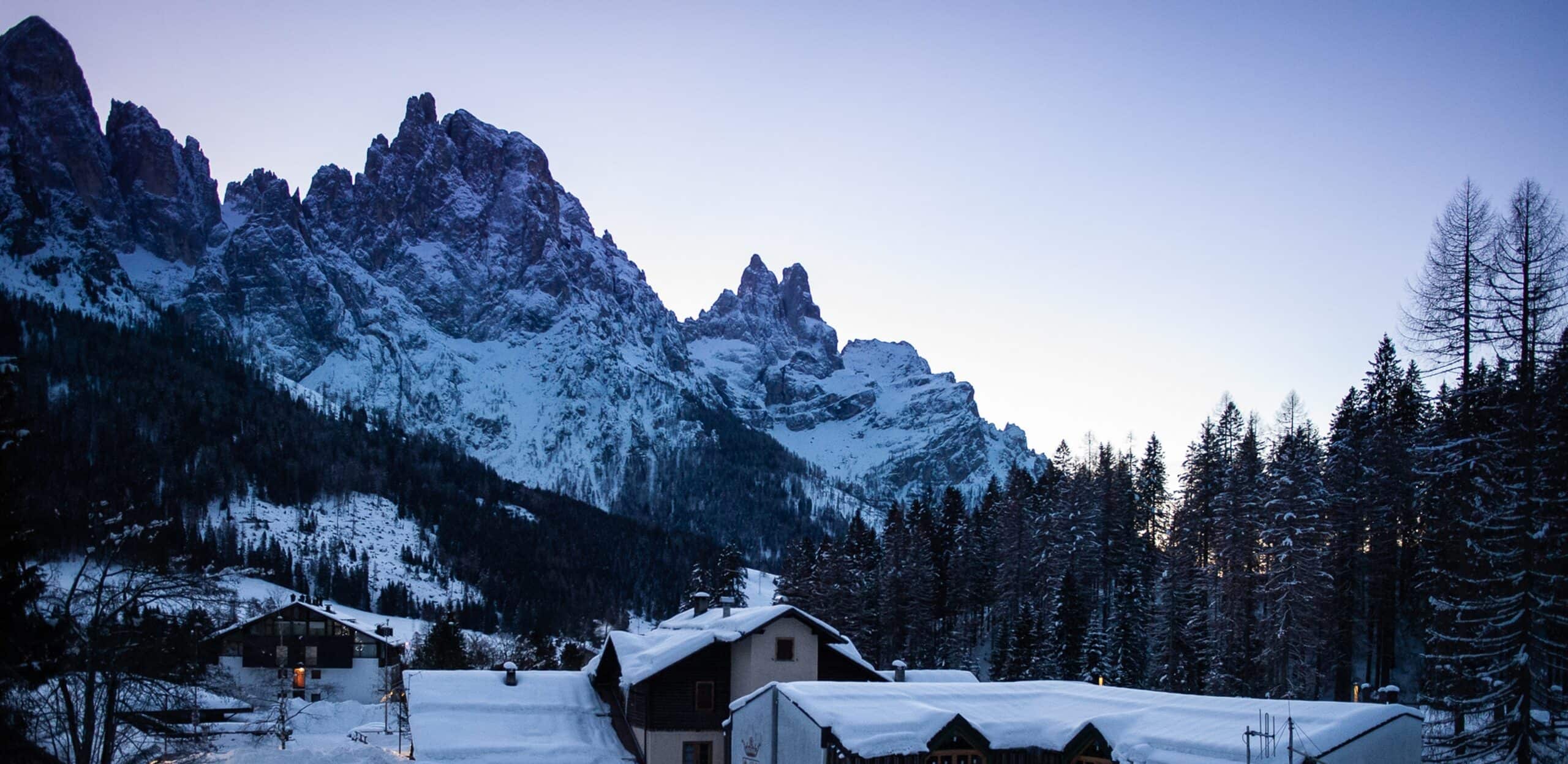 Case innevate in primo piano, foresta di conifere e alte montagne rocciose innevate sullo sfondo