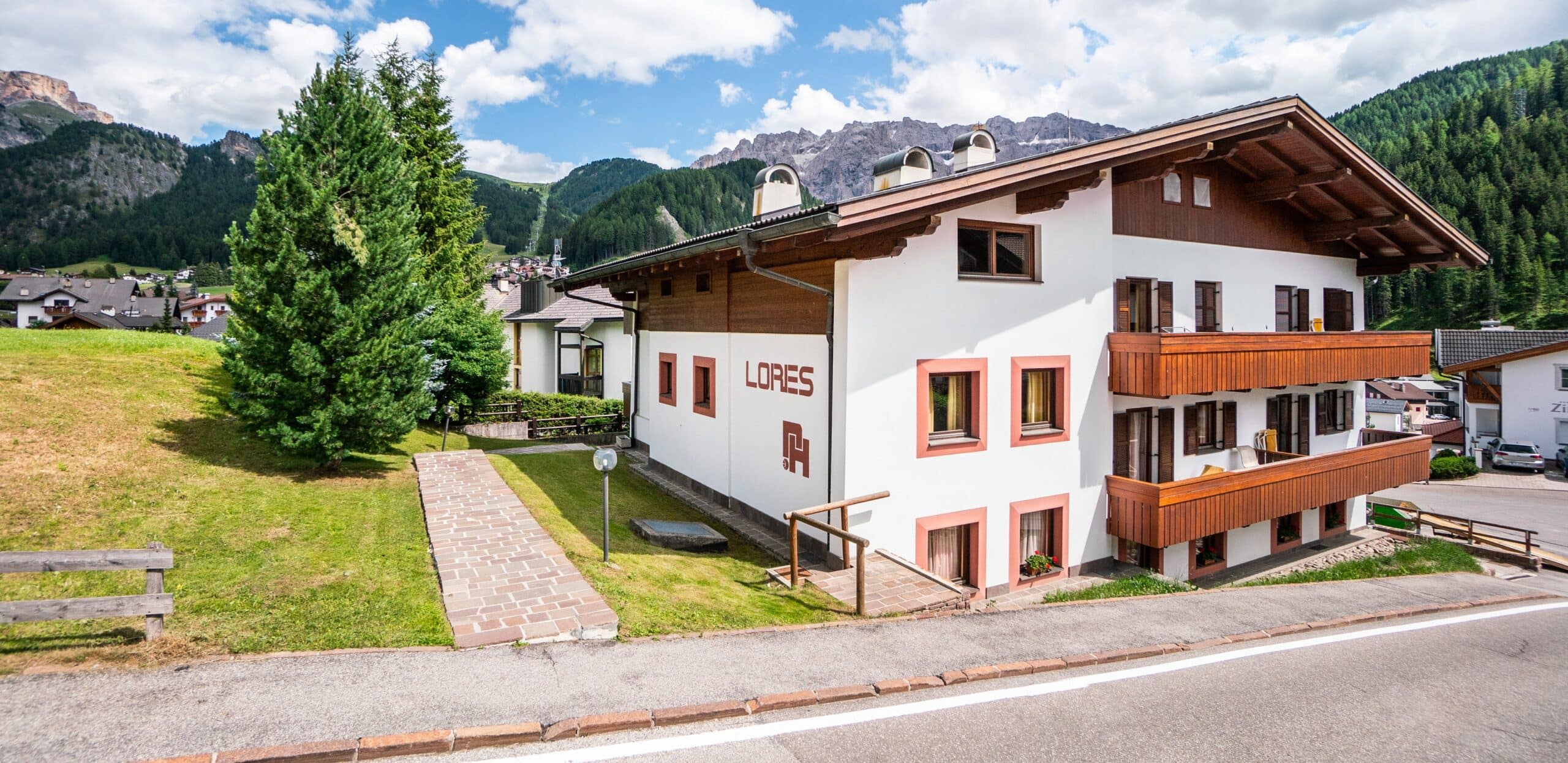 Edificio LORES con balconi in legno, prato davanti e montagne boschive sullo sfondo